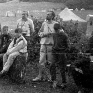 Group gathered around campfire in outdoor camping setting.