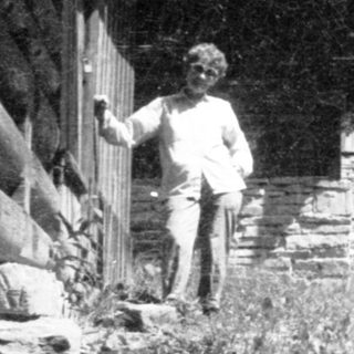 Rural scene with person standing near rustic stone house.