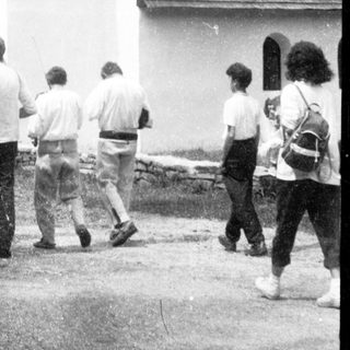 Group visiting small white church in forested area.