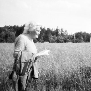 Woman reading in tall grass near old building.