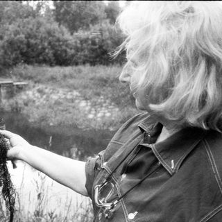 Person holding aquatic plant near water.