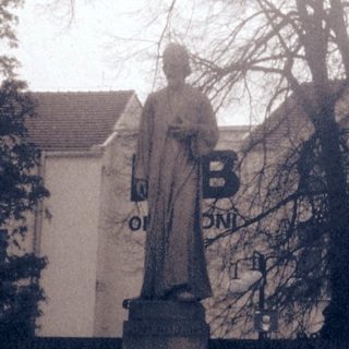 Statue of a robed figure in outdoor setting.