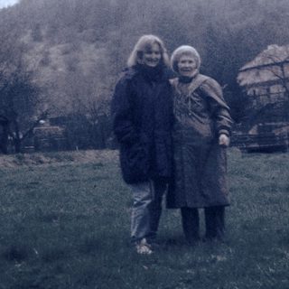 Two women standing outdoors near historic hilltop castle ruins.