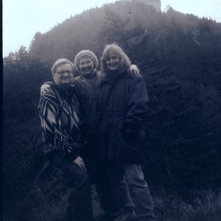 Three people posing together near a castle on a hill.