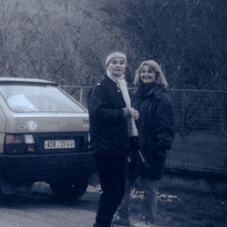 Two people standing beside an old car near rocky terrain.