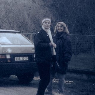 Two people standing beside an old car near rocky terrain.