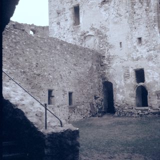 Medieval stone courtyard with arched doorways and rough walls.