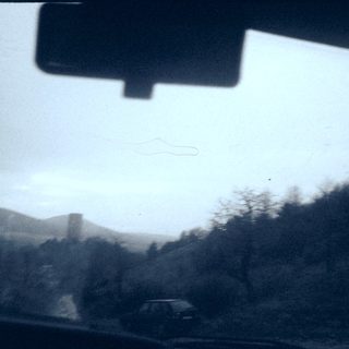 Blurry road view with distant car, hills, and sky.