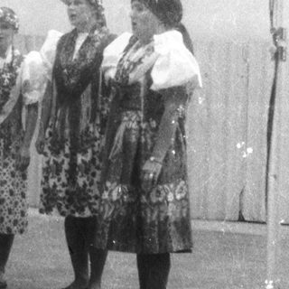 Group of women in traditional folk costumes singing on stage.