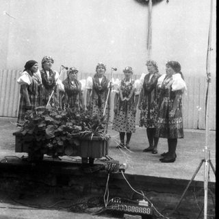 Group of women in traditional folk costumes singing on stage.
