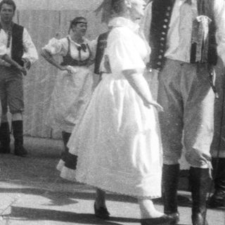 Traditional folk group performing outdoors with singing and dancing.