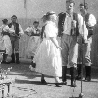 Traditional folk group performing outdoors with singing and dancing.