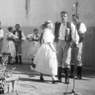 Traditional folk group performing outdoors with singing and dancing.