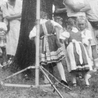 Group of people and children gathered around an old-fashioned telephone booth.