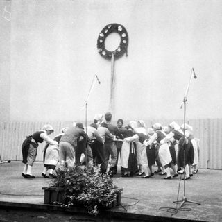 Group singing around large decorated pole.