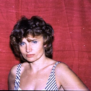 Woman in striped swimsuit against red backdrop.