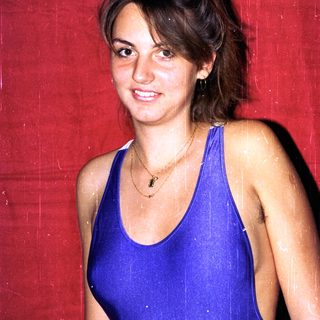 Woman smiling in blue swimsuit against red background.