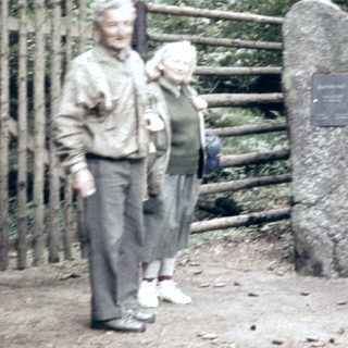 Three people and a dog near a memorial rock.