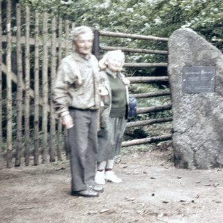 Three people and a dog near a memorial rock.