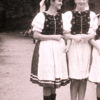 Four women in traditional folk dresses posing outdoors.