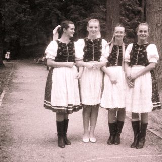 Four women in traditional folk dresses posing outdoors.