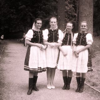 Four women in traditional folk dresses posing outdoors.