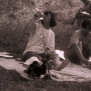 People relaxing outdoors on a picnic blanket in a wooded area.