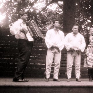 Traditional folk group performing outdoors with accordion and costumes.