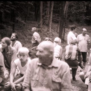 Group of people gathered outdoors in forested area.