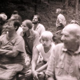 Group of people gathered outdoors in forested area.