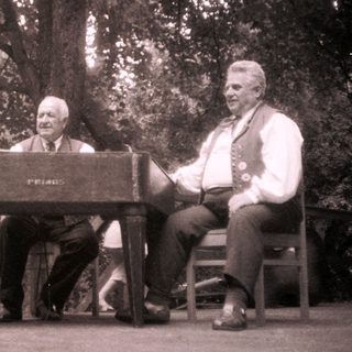Three men playing piano and singing outdoors.