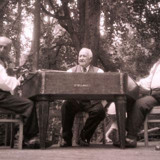 Three men playing piano and singing outdoors.