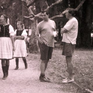 Group posing outdoors in traditional folk attire near vintage vehicle.