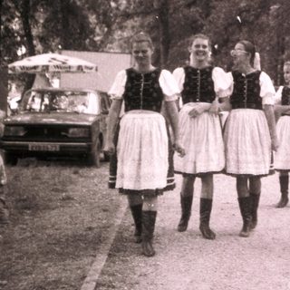Group posing outdoors in traditional folk attire near vintage vehicle.