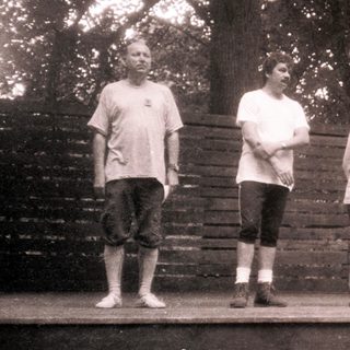 Group of men posing outdoors on wooden platform.