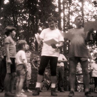 Group of children and adults outdoors, participating in a reading activity.