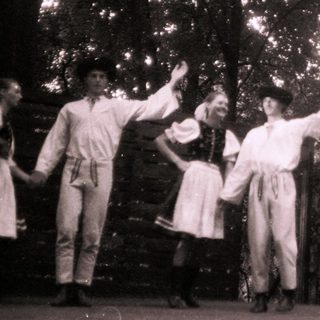 Traditional folk dancers in rural attire performing outdoors.