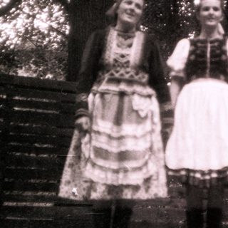 Three women in traditional folk dresses posing outdoors.