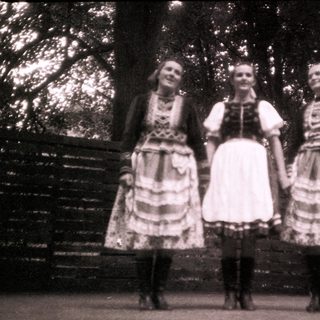 Three women in traditional folk dresses posing outdoors.