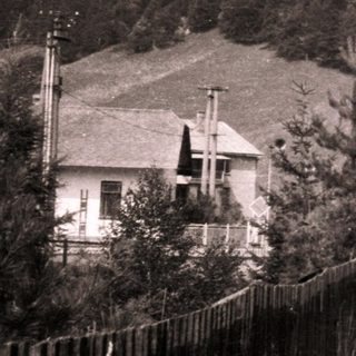 Rural roadside entrance to small building near forested hillside.