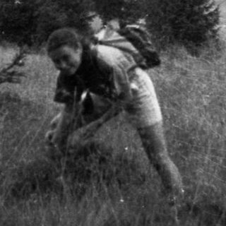 Person hiking through forested grassy terrain.