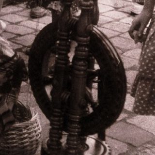 Woman spinning yarn on traditional spinning wheel.