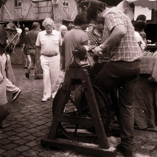 People operating traditional spinning wheel outdoors at fair.