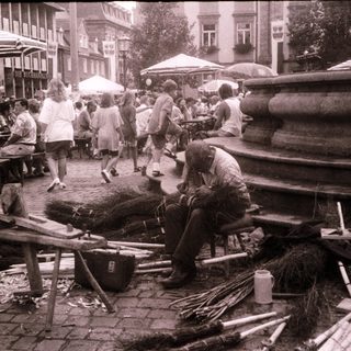 Street vendor sharpening sticks near busy outdoor seating area.