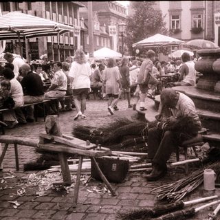 Street vendor sharpening sticks near busy outdoor seating area.