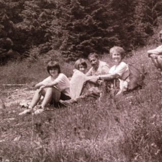 Four children sitting together outdoors in a forested area.