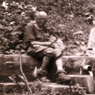 Three people resting on makeshift wooden bench in rugged forest terrain.