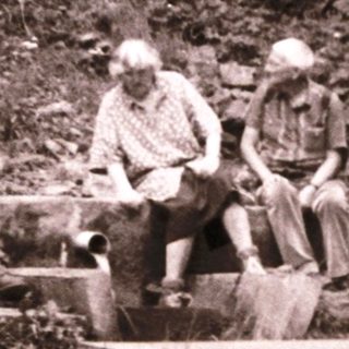 Three people resting on makeshift wooden bench in rugged forest terrain.