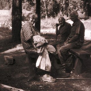 Three people sitting together outdoors in a wooded area.