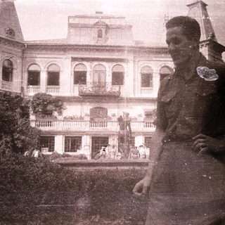 Military officer in front of colonial-era mansion.